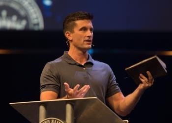 A man speaks on a large stage holding a Bible.