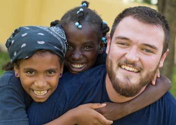 A man works with 2 children on a missions trip.