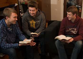 三个男学生聚集在一间灯光柔和的宿舍里学习圣经