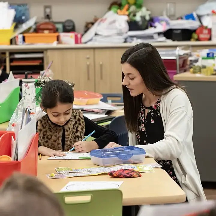 女教师在桌子旁用彩色铅笔画画，正在给一个年轻的学生讲课