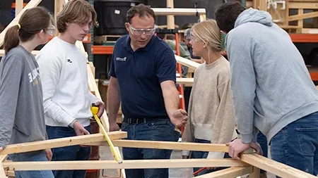 Professor instructing students in a engineering lab building a wooden structure.