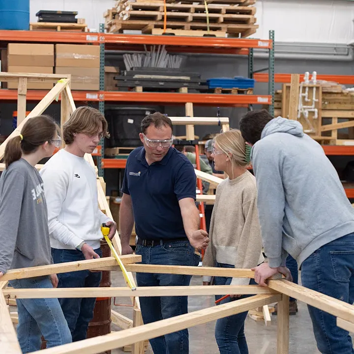 Professor instructing 机械 engineering students building a wooden structure.