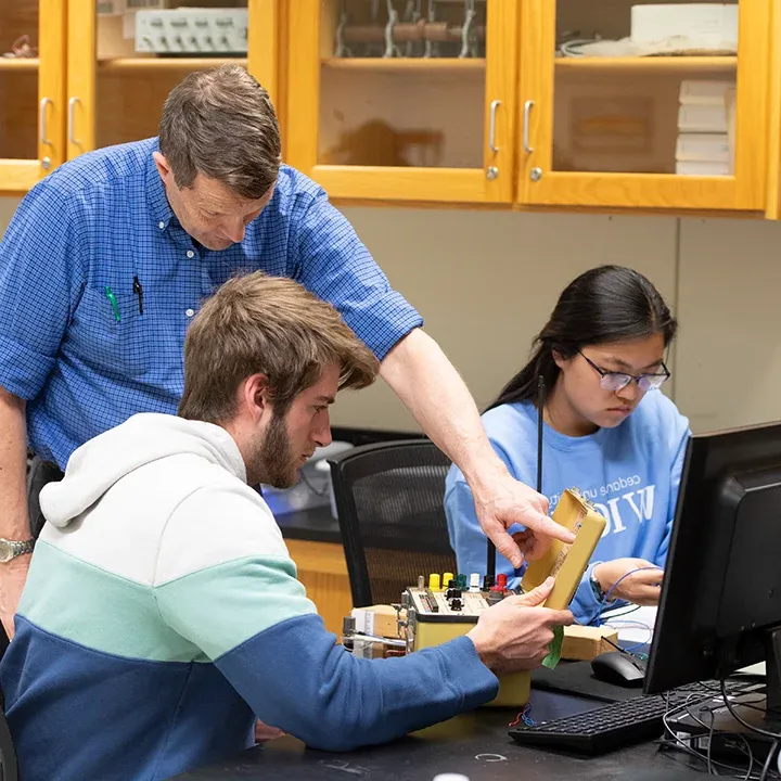 Professor working 与 students in an electronics lab.