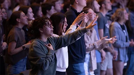 Students raising hands in worship during chapel.
