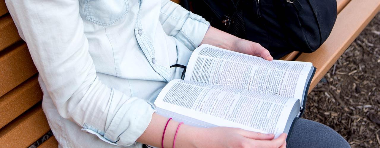 Female student reading her Bible on a park bench