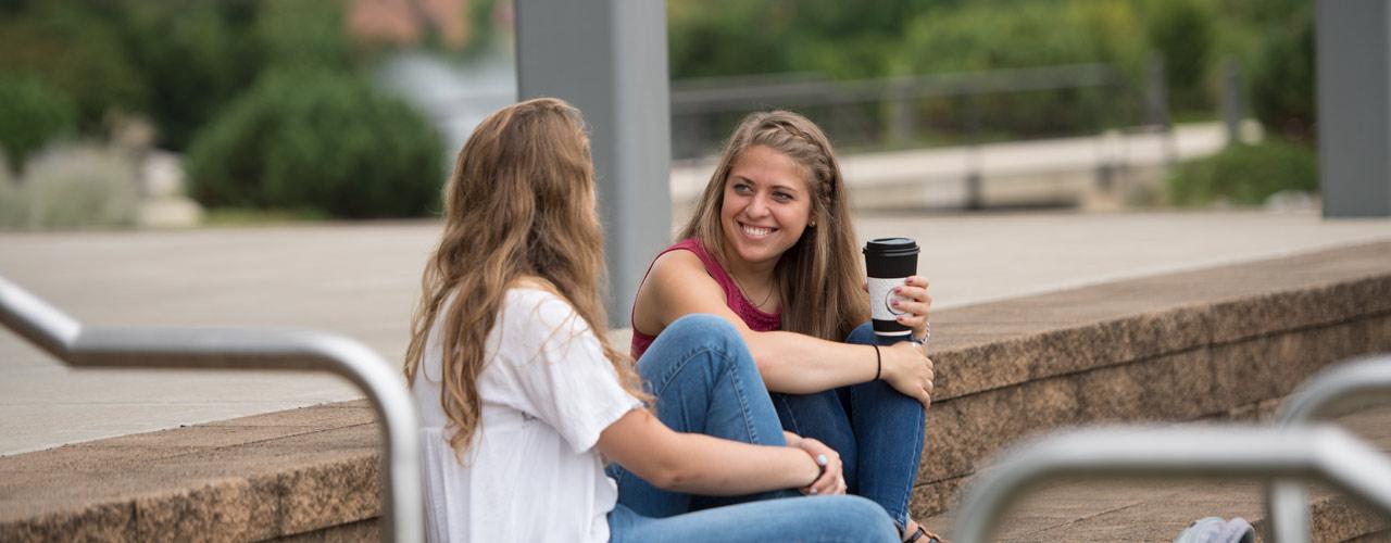 在圣经和神学研究中心外的石阶上，两名塞达维尔女学生端着咖啡微笑着