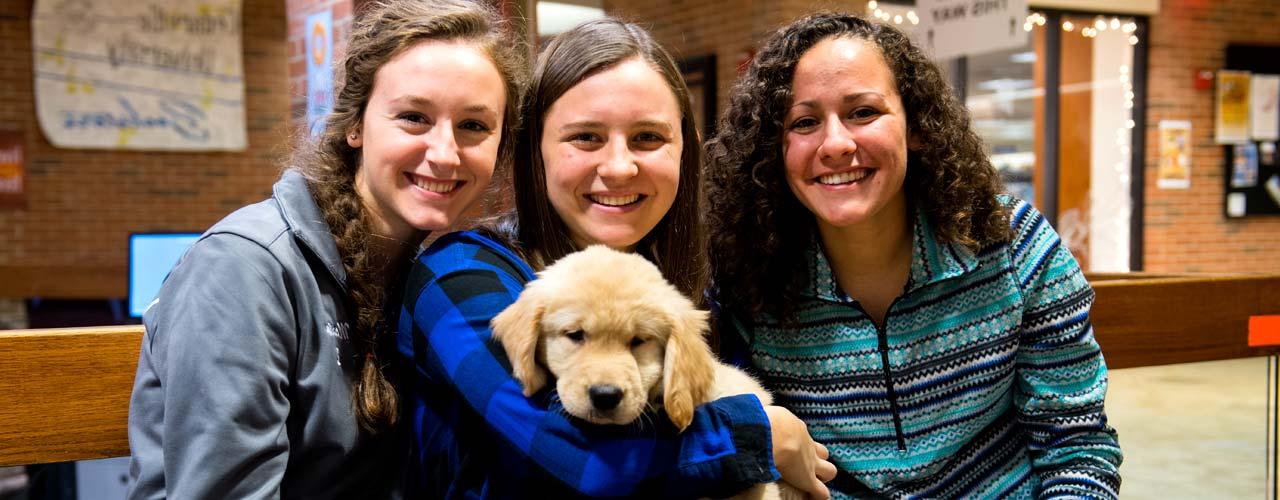 三名女学生在史蒂文斯学生中心抱着一只小狗