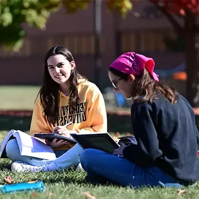 阳光明媚的一天，女学生坐在草坪上学习.