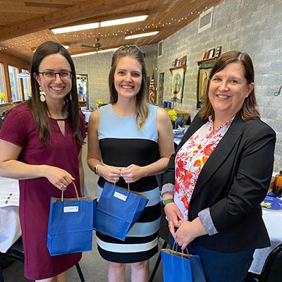 Three female alumni standing with gift bags