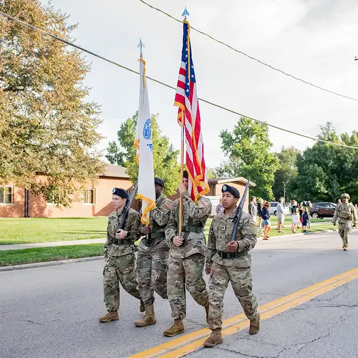 四名身着迷彩服的军人手持旗帜和步枪在街头游行.
